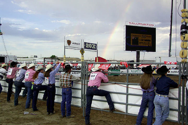 A rainbow graces the sky as participants watch the action in the rough stock arena.